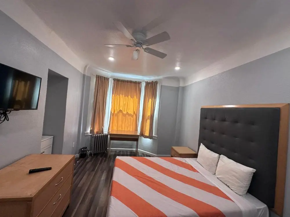 A wide view of a hotel room with a large bed, TV, and window.
